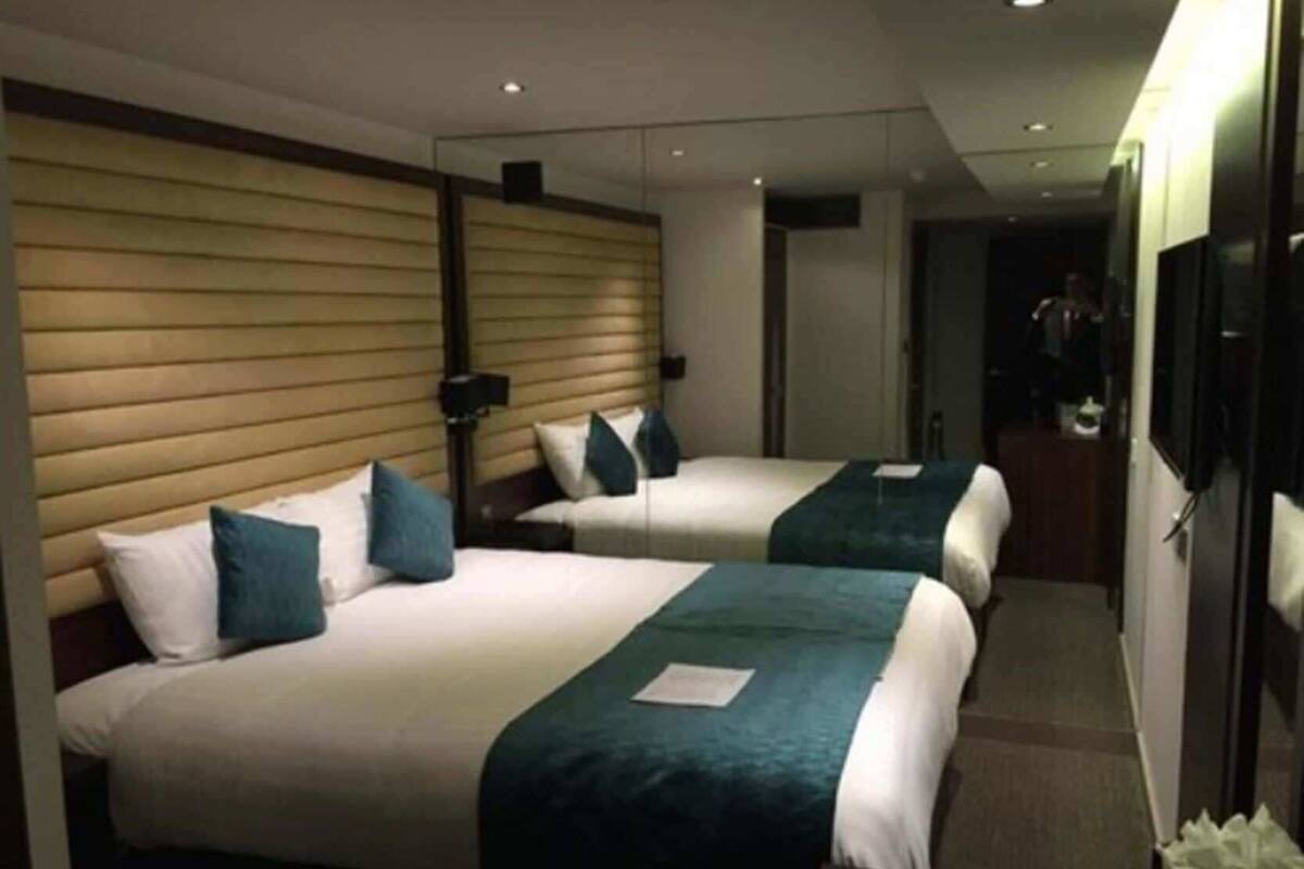A hotel room with two beds, a wooden headboard, a bedside table, a lamp, and a mirror.