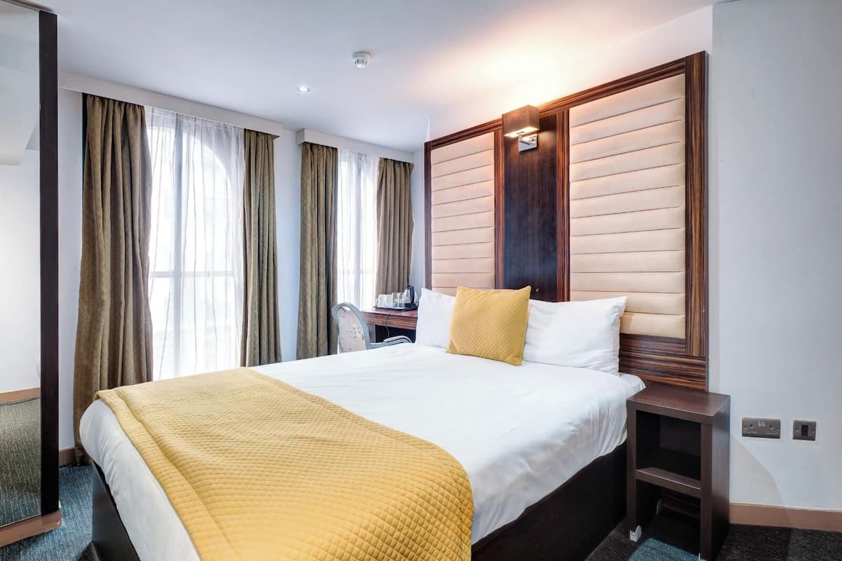 A hotel room with a large bed, a desk, and a chair.