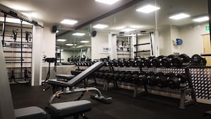 Een sportschool met krachttrainingsapparatuur, spiegels en een bank.