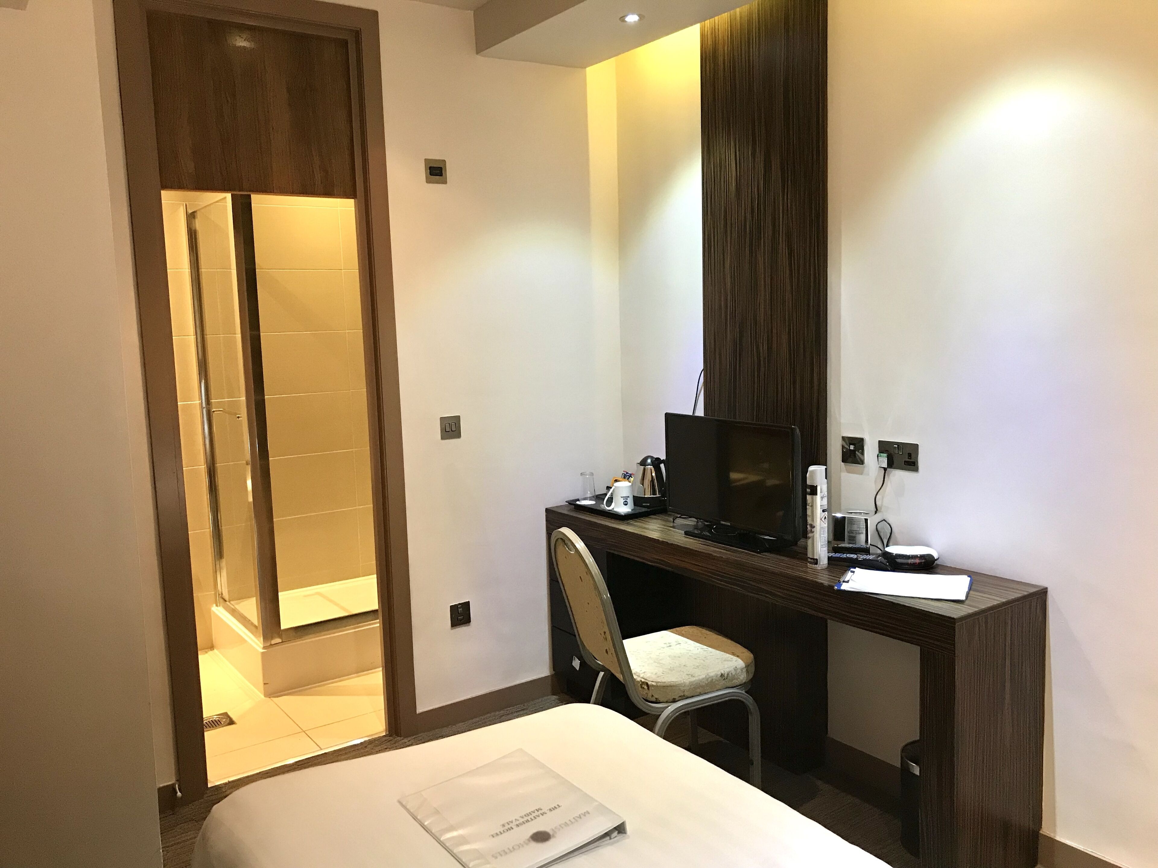 A hotel room with a bed, a desk with a computer, a chair, and a shower area.