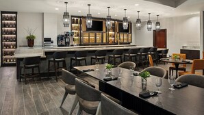 A modern dining area with a long table, multiple chairs, and a bar with a wine display. - Bloomington-Normal Marriott Hotel & Conference Center (Normal)