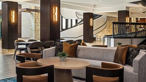 A modern lobby with a round wooden table, grey sofa, and dark wooden chairs. - Bloomington-Normal Marriott Hotel & Conference Center (Normal)