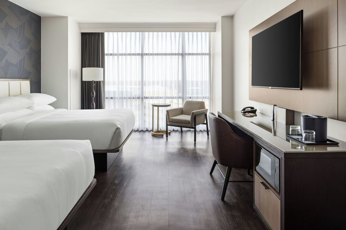 A hotel room with two beds, a desk, a chair, a TV, and a window with curtains.