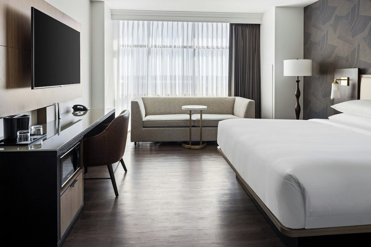A hotel room with a bed, a sofa, a desk, a TV, and a lamp.
