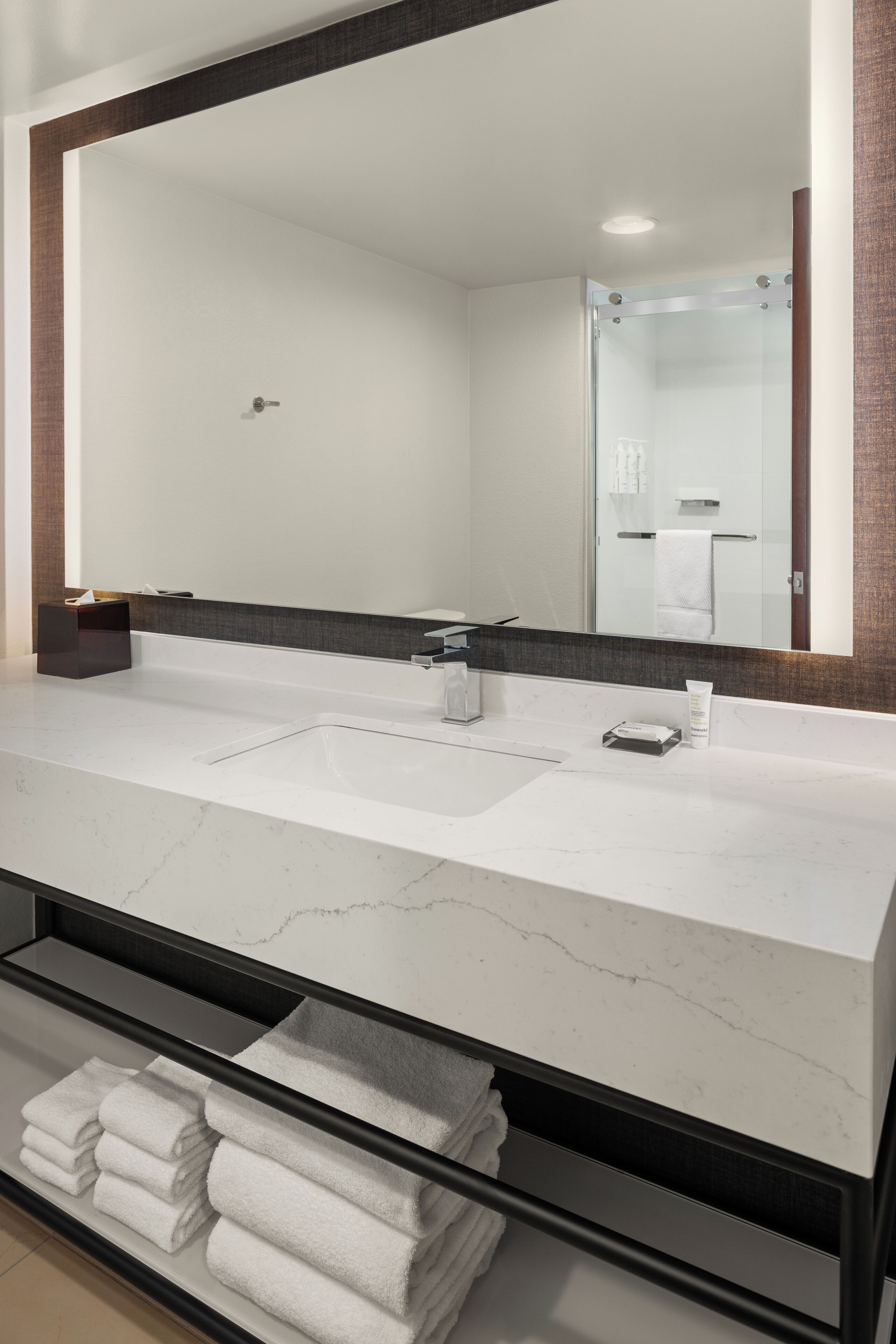 Une salle de bain moderne avec un grand miroir, un plan de toilette en marbre blanc et un porte-serviettes où sont pliés des serviettes.