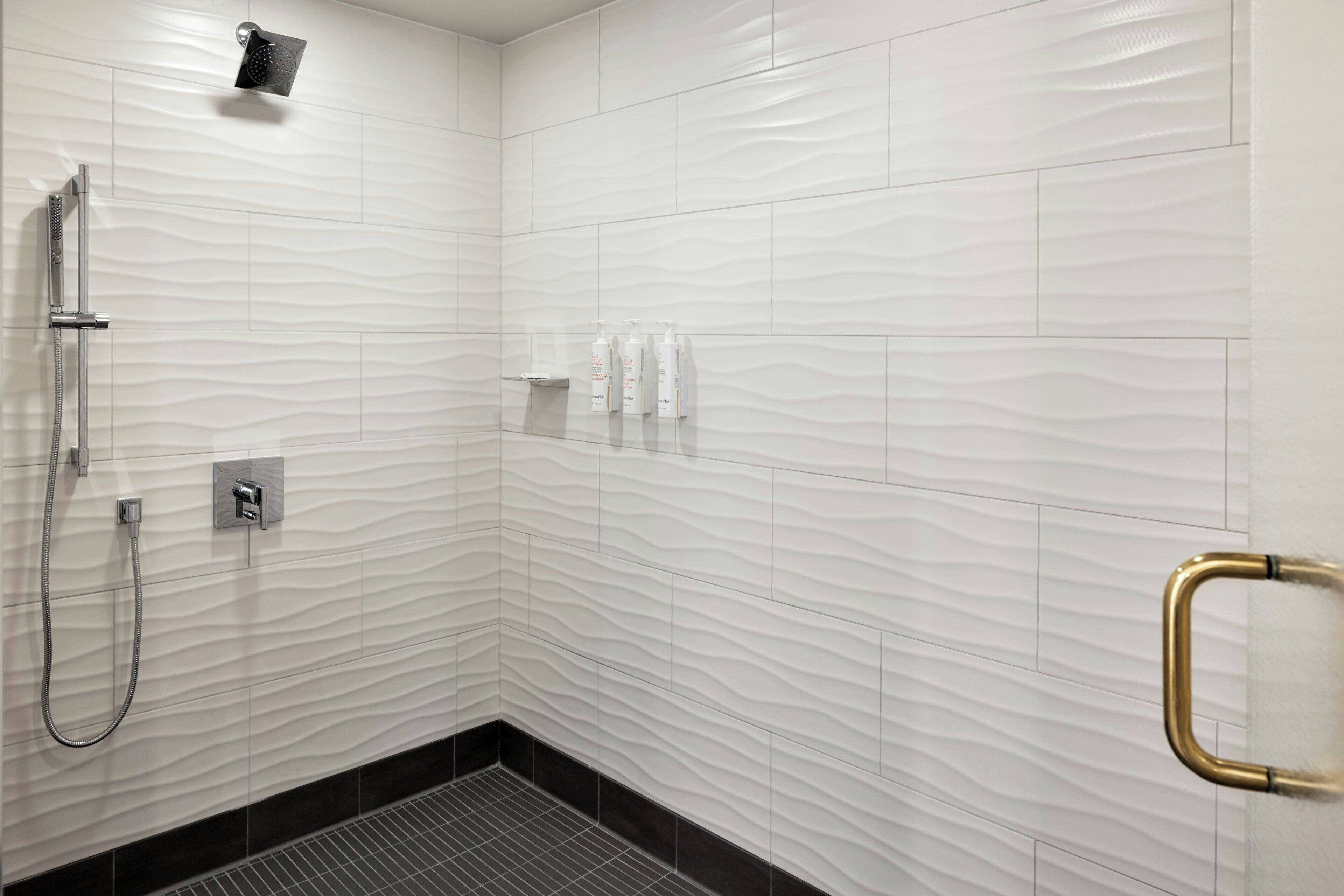 Un baño moderno con ducha, secamanos y artículos de aseo en un estante.