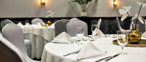 Un comedor con mesas redondas dispuestas para cuatro personas, cada una con mantel blanco, cubiertos y cristalería.