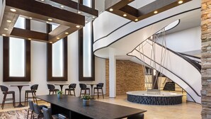 A modern hotel lobby with a large conference table, multiple chairs, a patterned carpet, and a spiral staircase. - Bloomington-Normal Marriott Hotel & Conference Center (Normal)