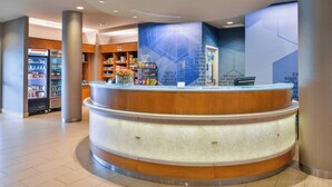 A reception area with a curved counter, a refrigerator stocked with beverages, and shelves with snacks. - SpringHill Suites by Marriott Ashburn Dulles North (Ashburn)