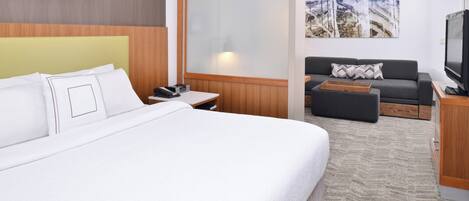 Habitación de hotel con una cama grande, un sofá, un televisor y un cabecero de madera.