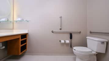 Et badeværelse med et hvidt toilet, en glasreol med håndklæder, et gelænder og en toiletpapirholder.