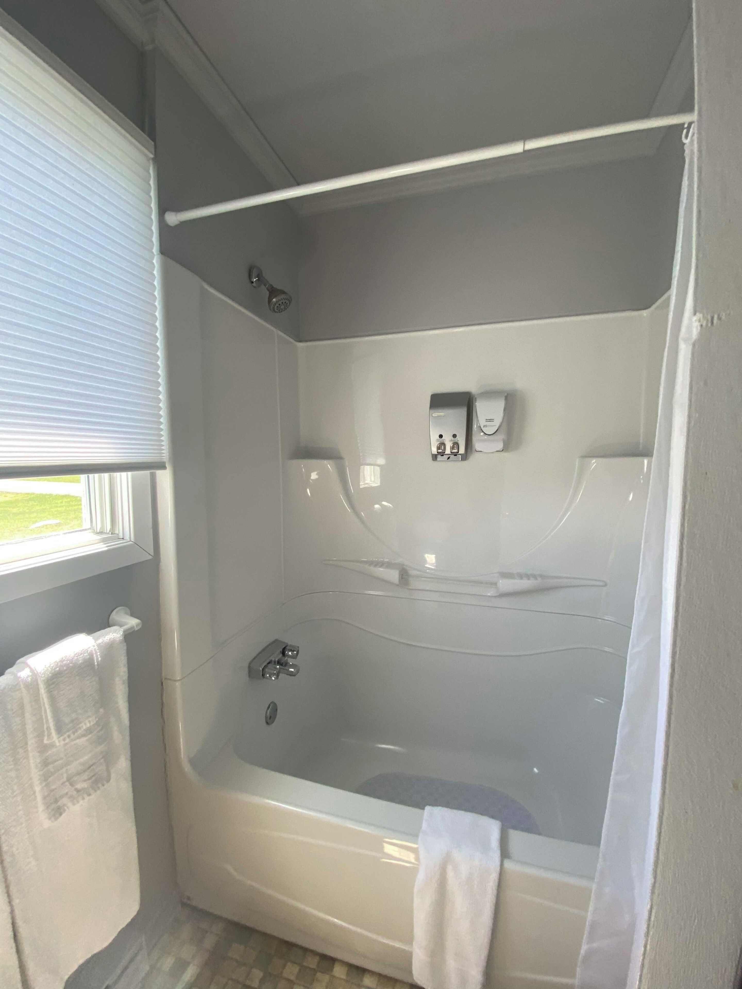 Un baño con bañera, cabezal de ducha, toallero y ventana.