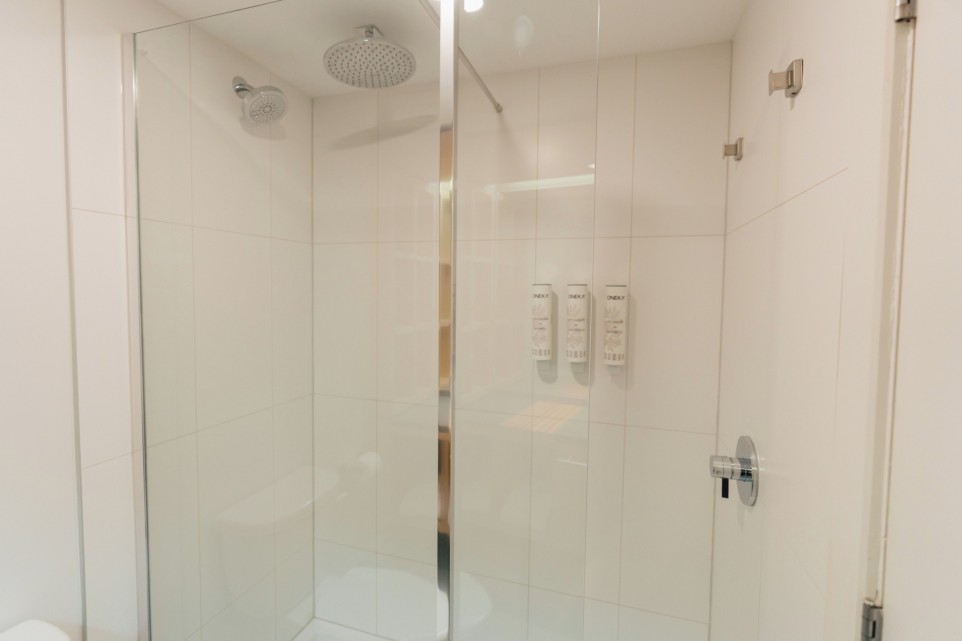 A glass-enclosed shower with a handheld showerhead, a control panel with buttons, and a wall-mounted towel rack.