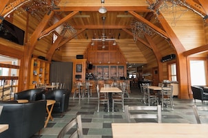 Um espaço amplo e interno com vigas de madeira, vários espaços de estar e um bar.