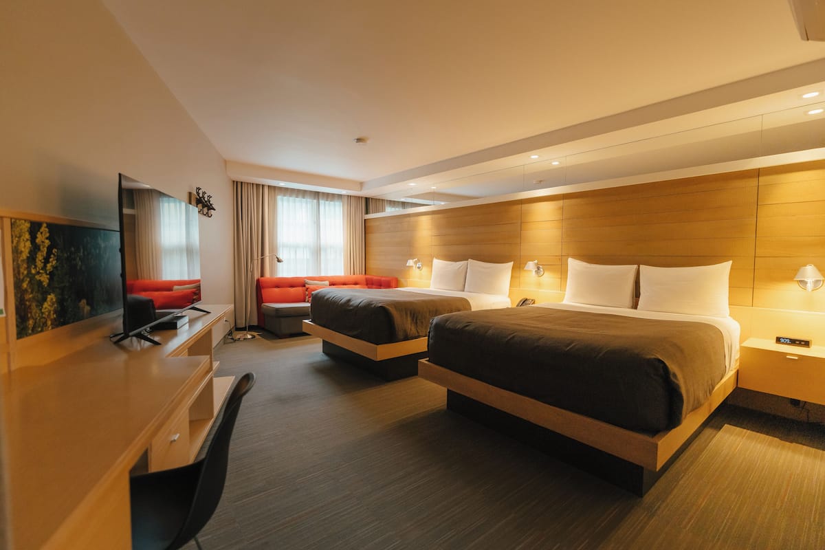A hotel room with two beds, a desk, a chair, and a TV.