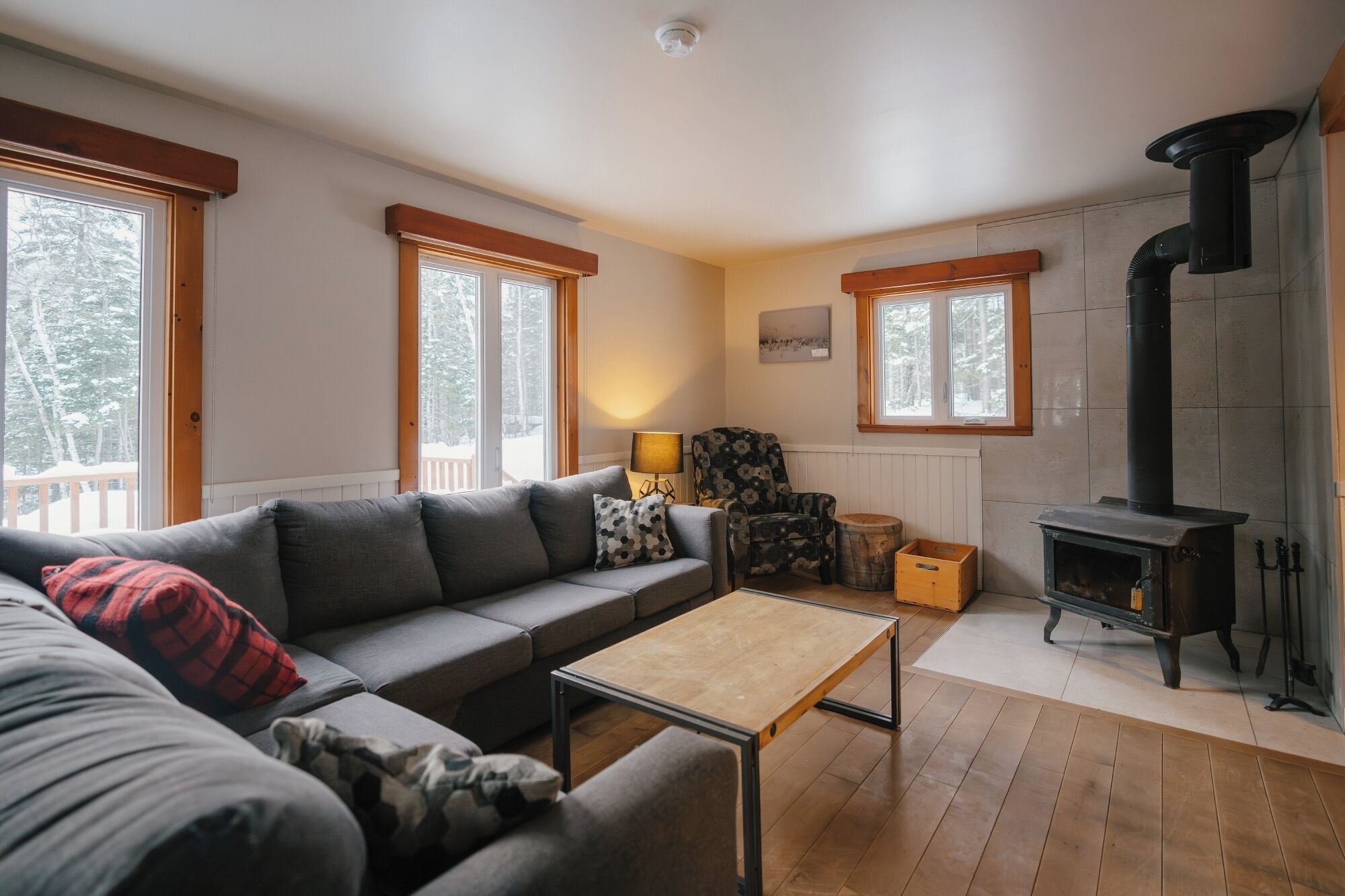 Una sala de estar acogedora con un sofá, una mesa de centro, una silla, una lámpara, una chimenea y ventanas amplias.