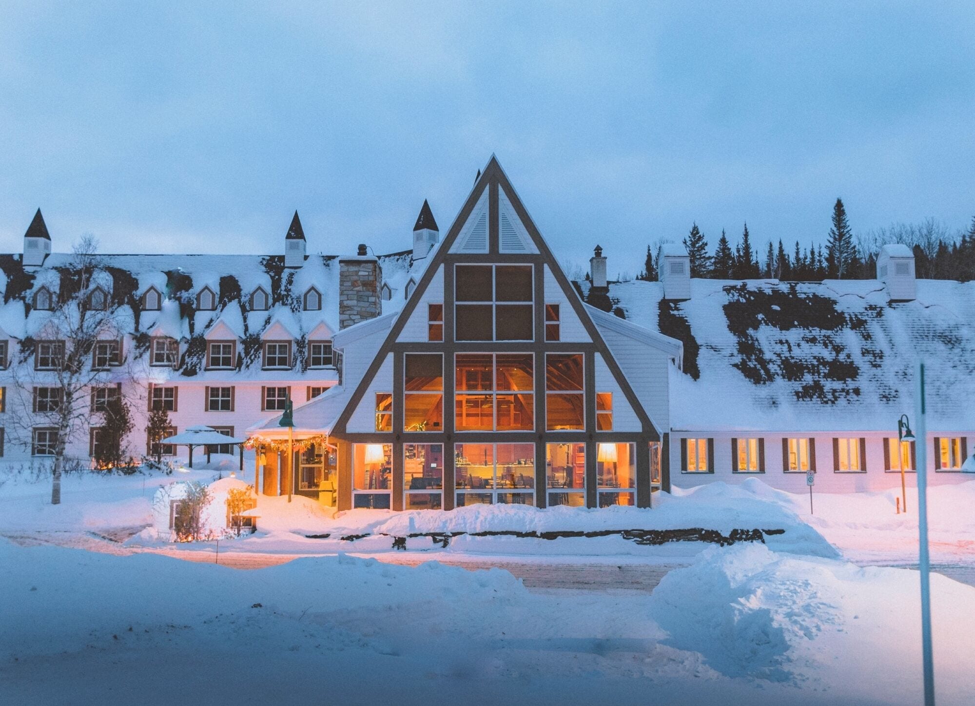 A snow-covered building with a prominent triangular roof, multiple windows, and a well-lit interior.