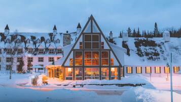 A snow-covered building with a prominent triangular roof, multiple windows, and a well-lit interior.