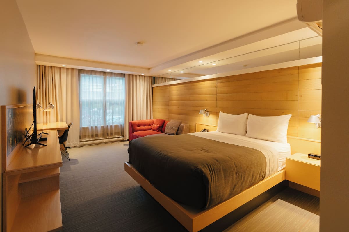 A modern hotel room with a large bed, a desk, and a red armchair.
