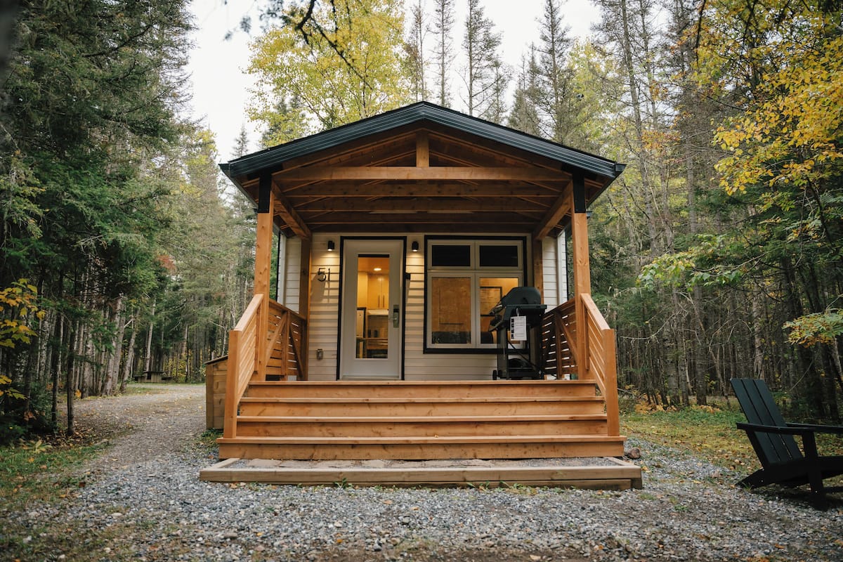 A wooden cabin with a porch, a staircase, and a door leading to the interior.