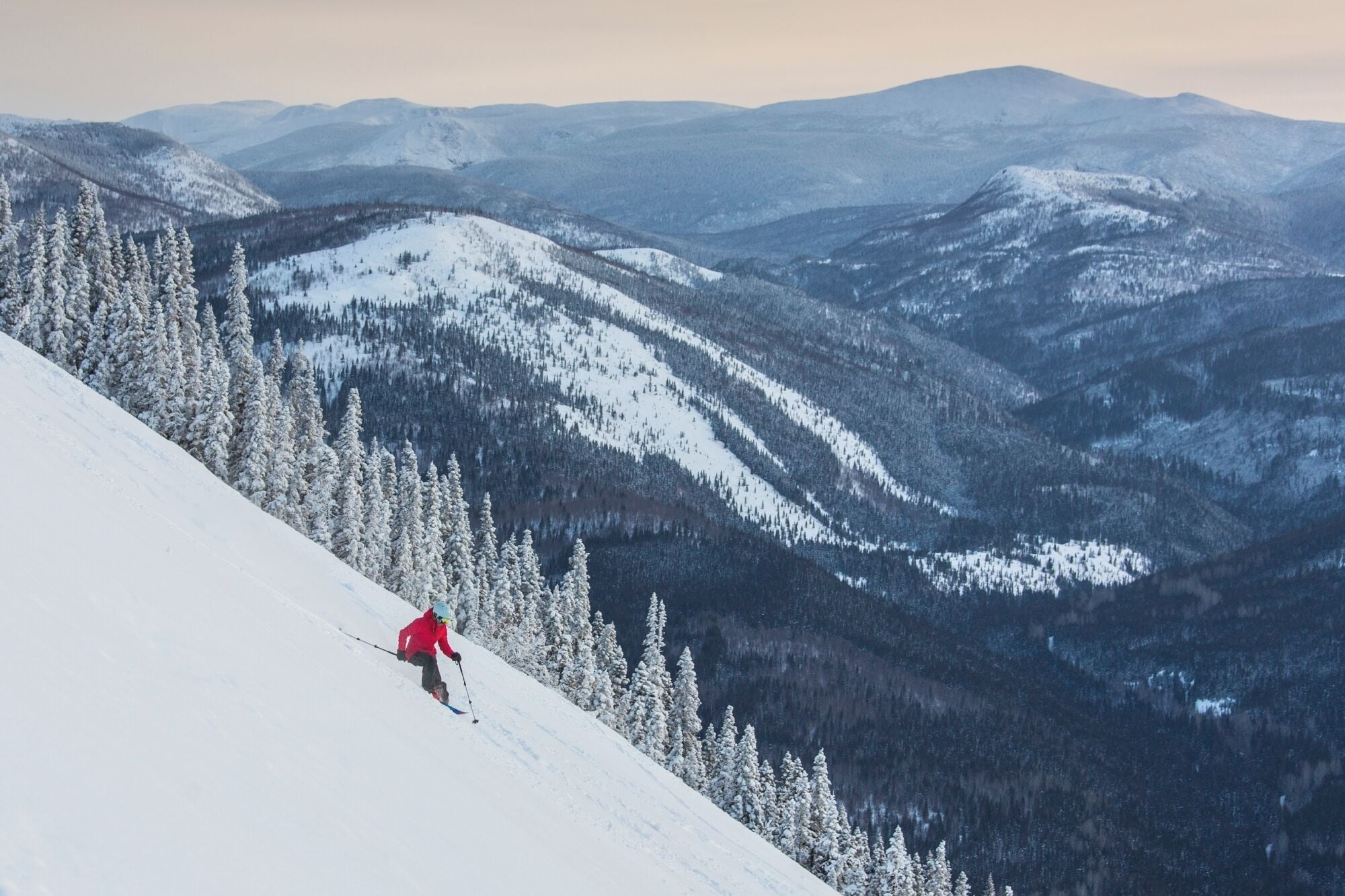 A snowy mountain landscape with a skier descending a slope.