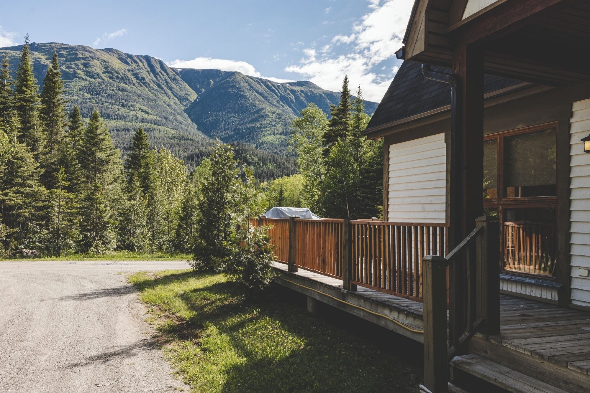 A cabin with a wooden deck, a covered barbecue area, and a view of a forested mountain range.