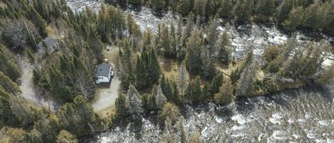 An aerial view of a cabin surrounded by dense forest and a river.