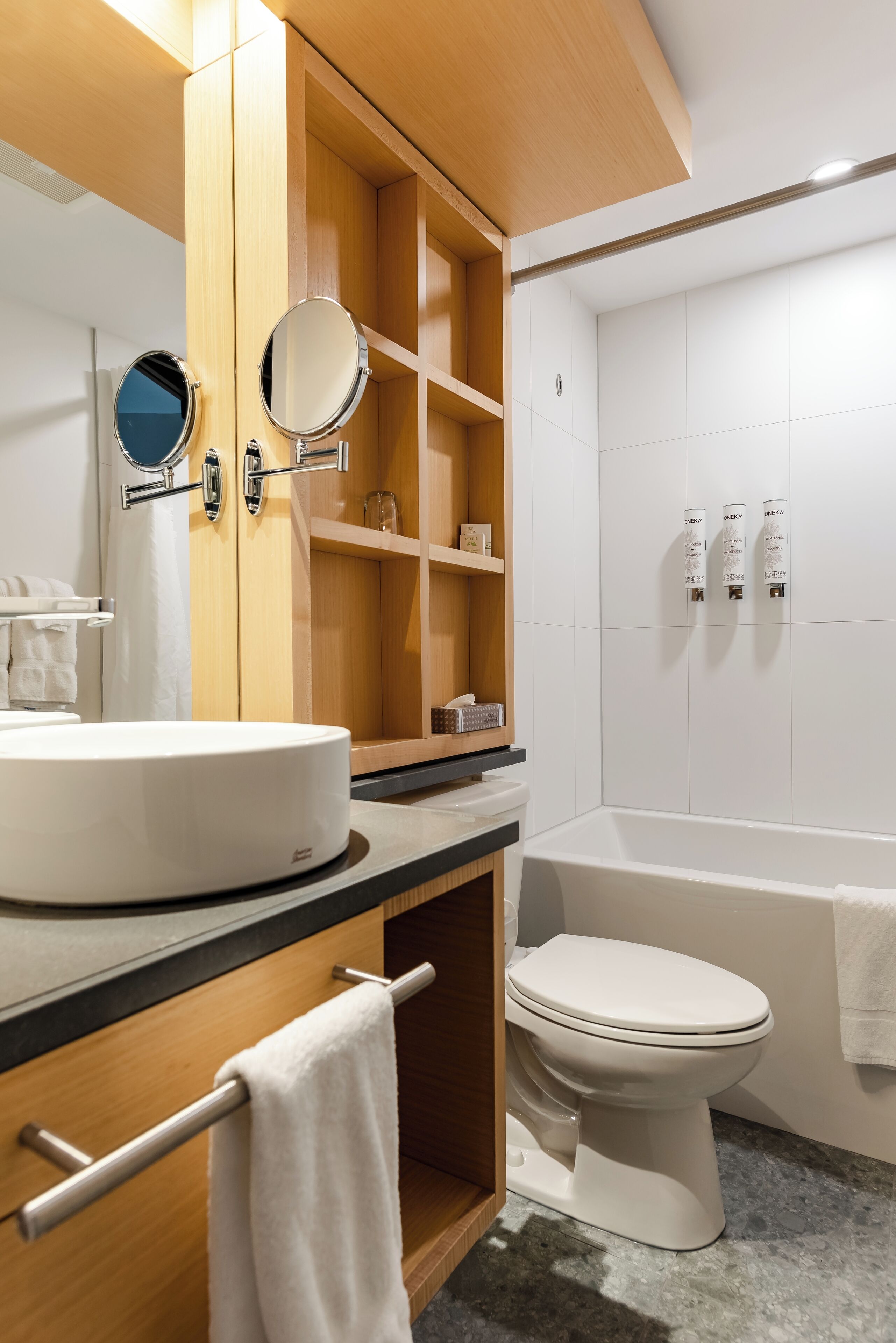 A modern bathroom with a wooden vanity, a round mirror, a white sink, and a white toilet.