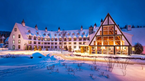 Un hotel grande de varios pisos con estilo arquitectónico europeo tradicional, que destaca por su amplia fachada de vidrio y un paisaje cubierto de nieve.