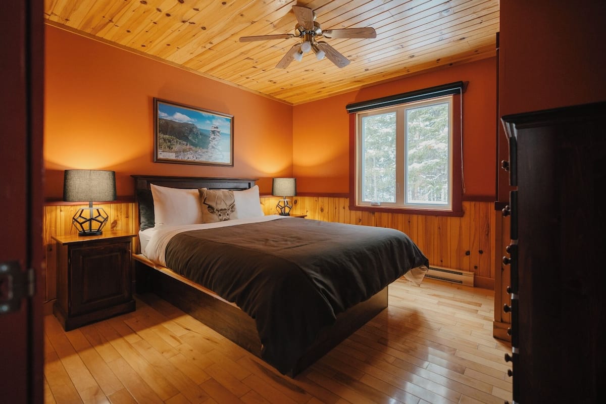 A bedroom with a bed, two bedside lamps, a ceiling fan, a window, and a door.