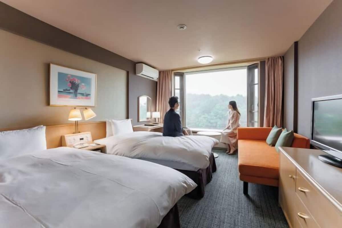 A hotel room with two beds, a sofa, a TV, and a large window.