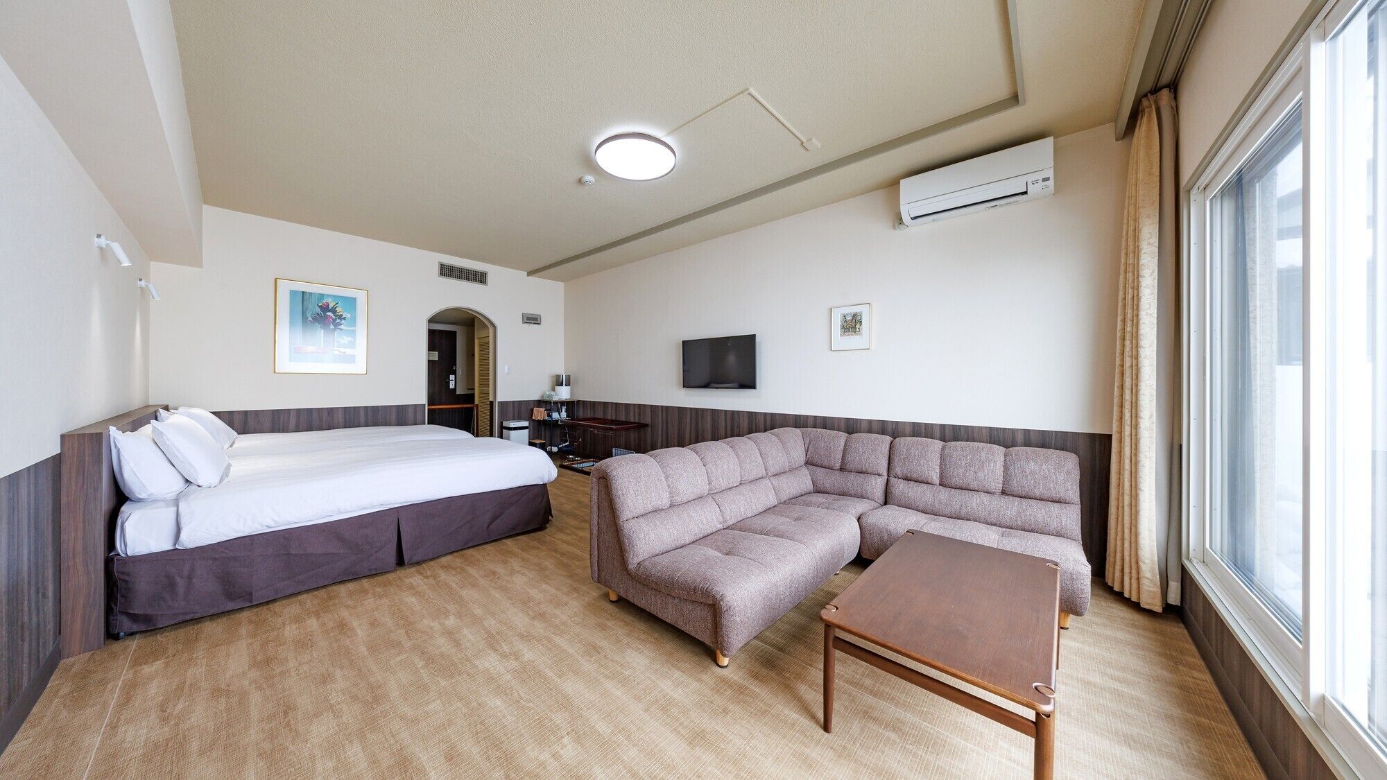 A hotel room with a bed, a sofa, a small table, a TV, and a window.
