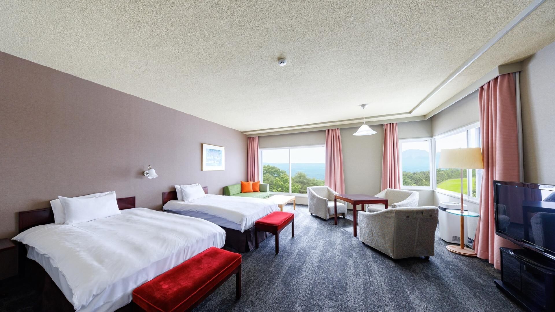 A hotel room with two beds, a sofa, a TV, and a view of the outdoors.