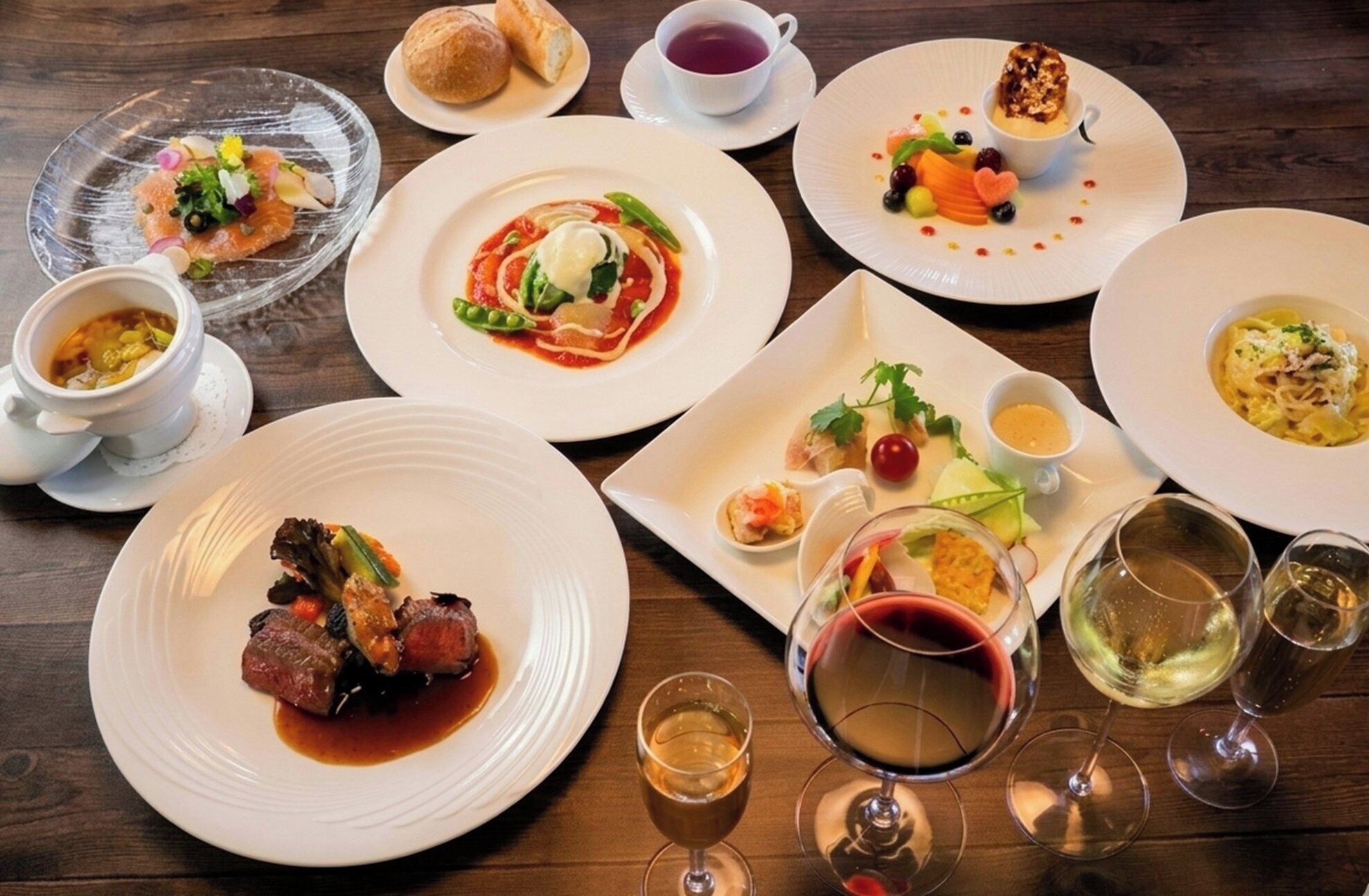 A variety of dishes and glasses of wine on a wooden table.