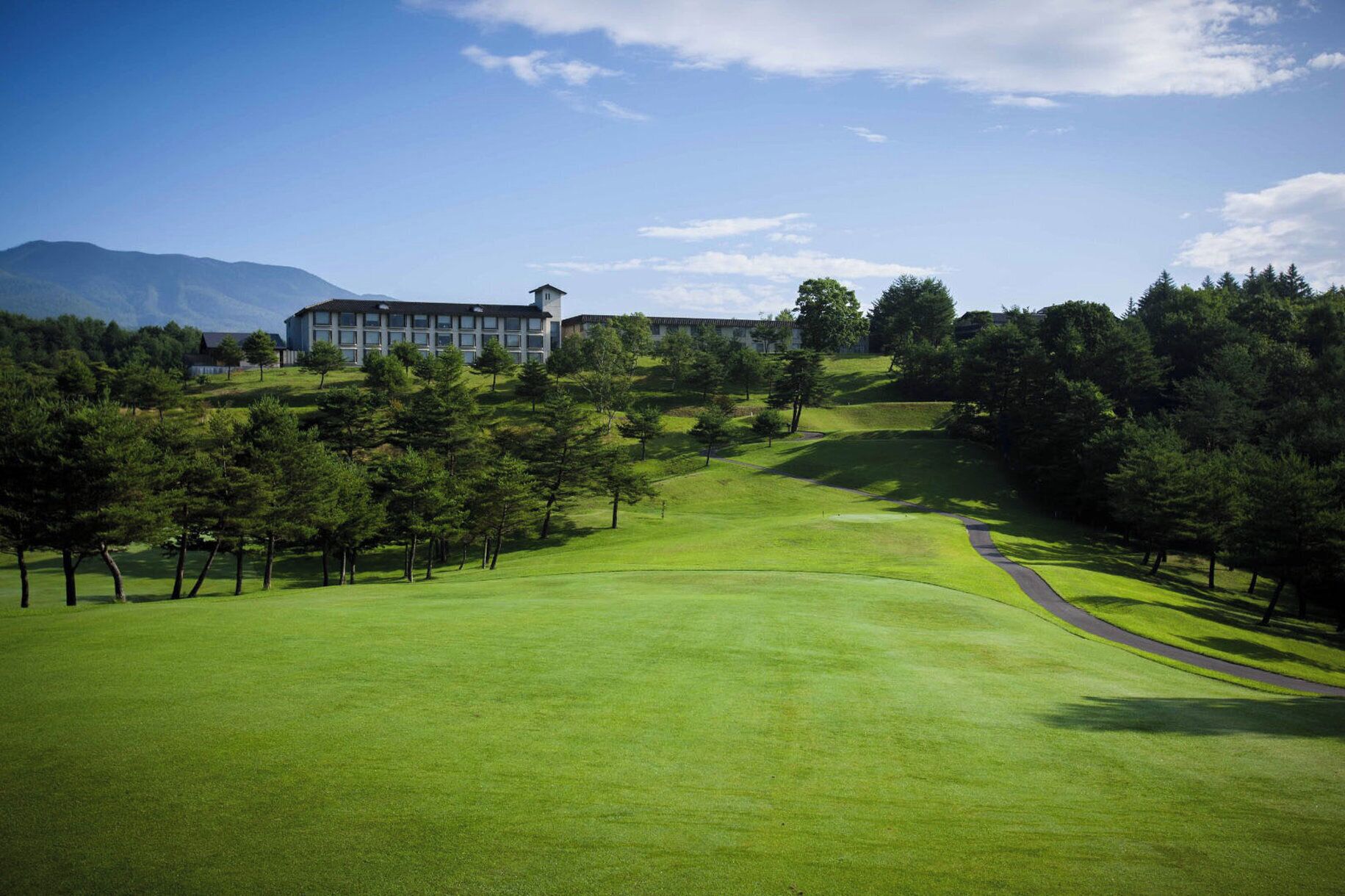 A golf course with a clubhouse, surrounded by trees and mountains.