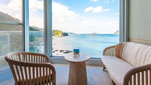 Un balcon agrémenté de fauteuils en osier et d’une petite table ronde, offrant une vue sur un paysage côtier sous un ciel dégagé.