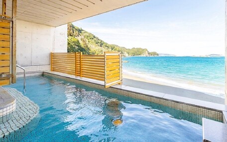 A hot tub with a wooden bench, a tiled floor, and a view of the beach and ocean.