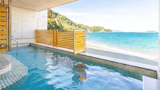 Un bain à remous avec un banc en bois, un sol carrelé et une vue sur la plage et l’océan.