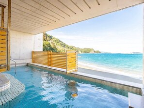 A hot tub with a wooden bench, a tiled floor, and a view of the beach and ocean.