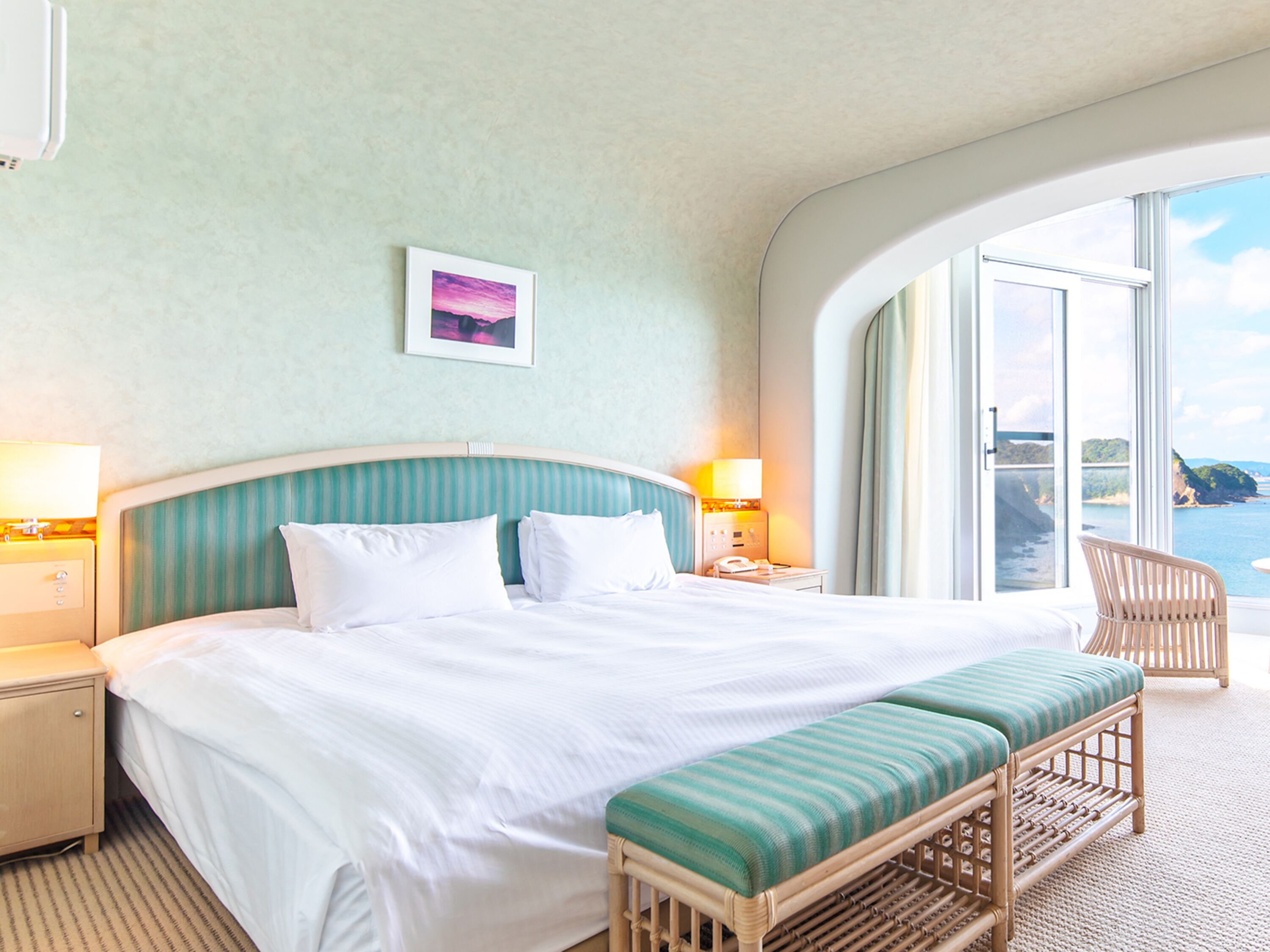 Ett hotellrum med en stor säng, en bänk, en stol och utsikt över havet.