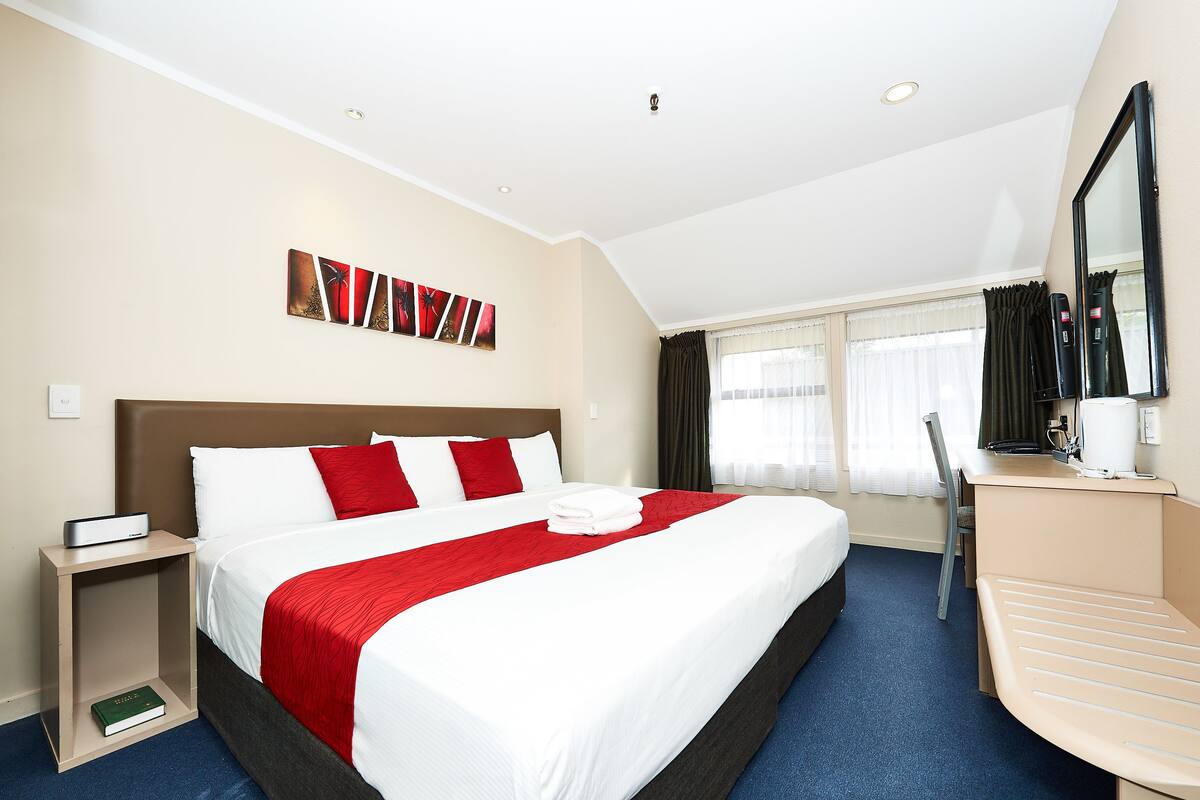 A hotel room with a large bed, a desk, a chair, and a mirror.