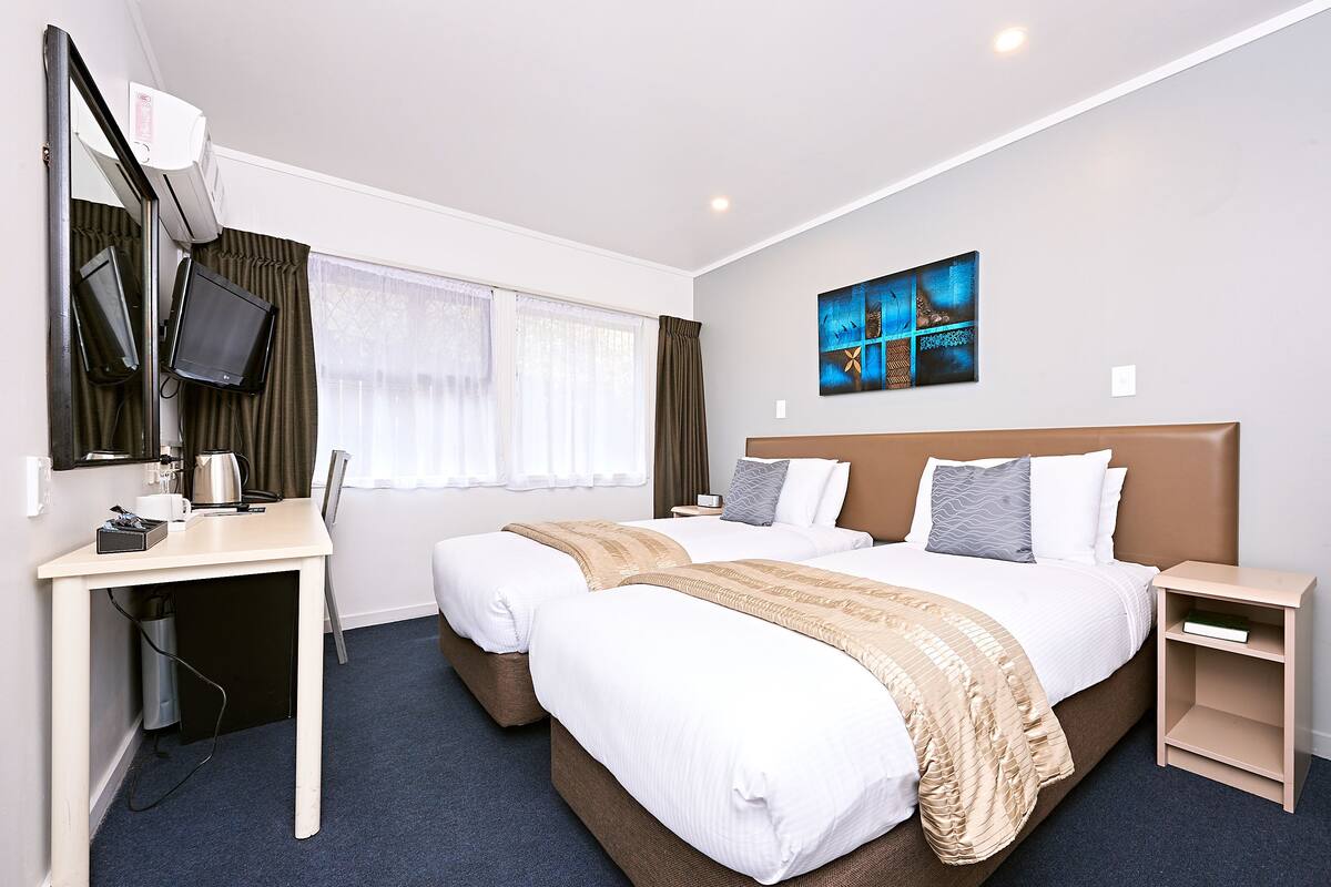 A hotel room with two beds, a desk, a TV, and a painting on the wall.