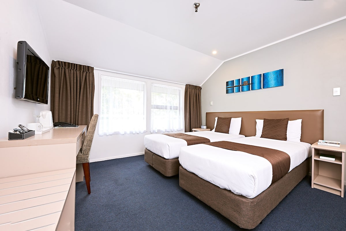 A hotel room with two beds, a desk, a TV, and a window with curtains.