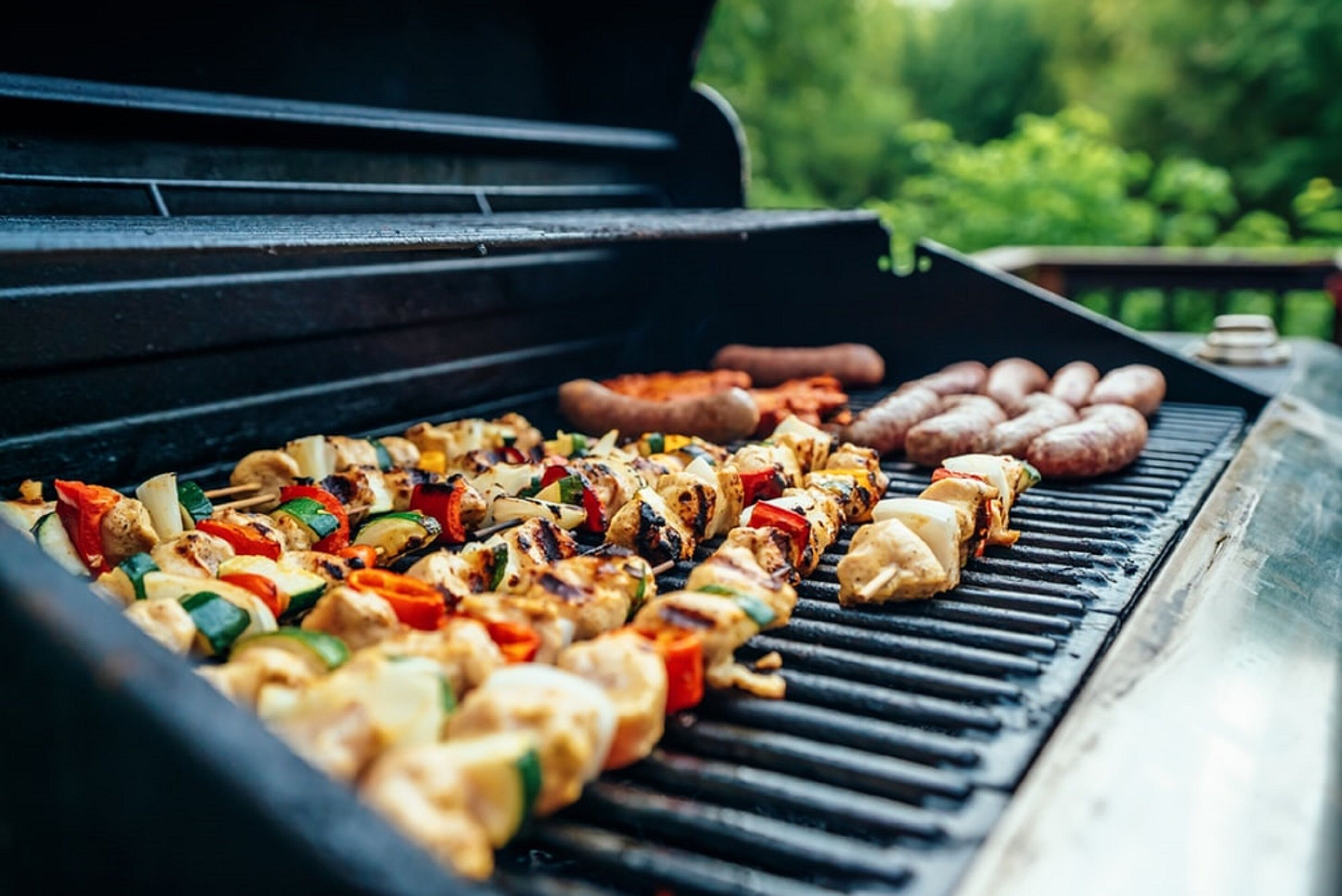 Una parrilla con brochetas de vegetales y carne, y salchichas asándose.