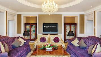 A luxurious living room with a chandelier, two sofas, a coffee table with a floral arrangement, and a flat-screen TV mounted on the wall.