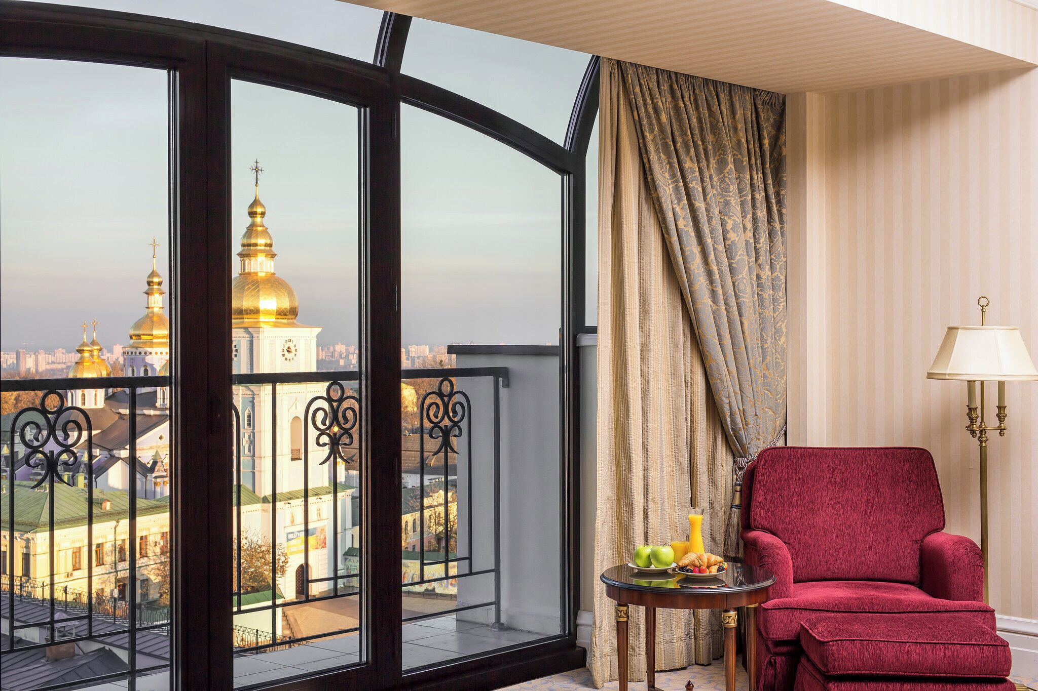 Una habitación con un sillón rojo, una mesa con desayuno y vistas a cúpulas doradas.
