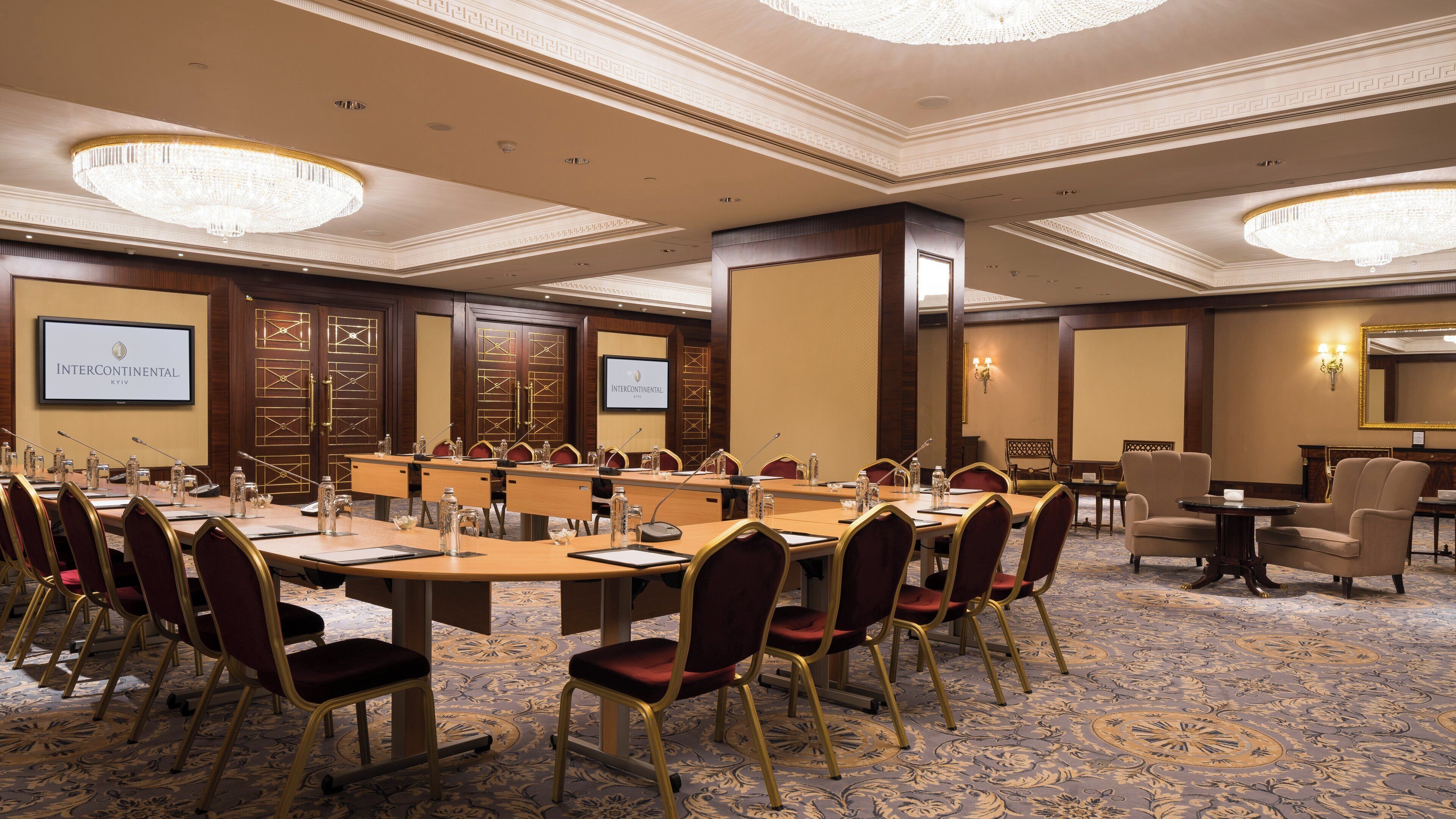 A conference room with a long table, chairs, a projector screen, and a large chandelier.