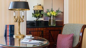 A wooden chair with a cushion, a round table with a lamp, books, and a vase with flowers.
