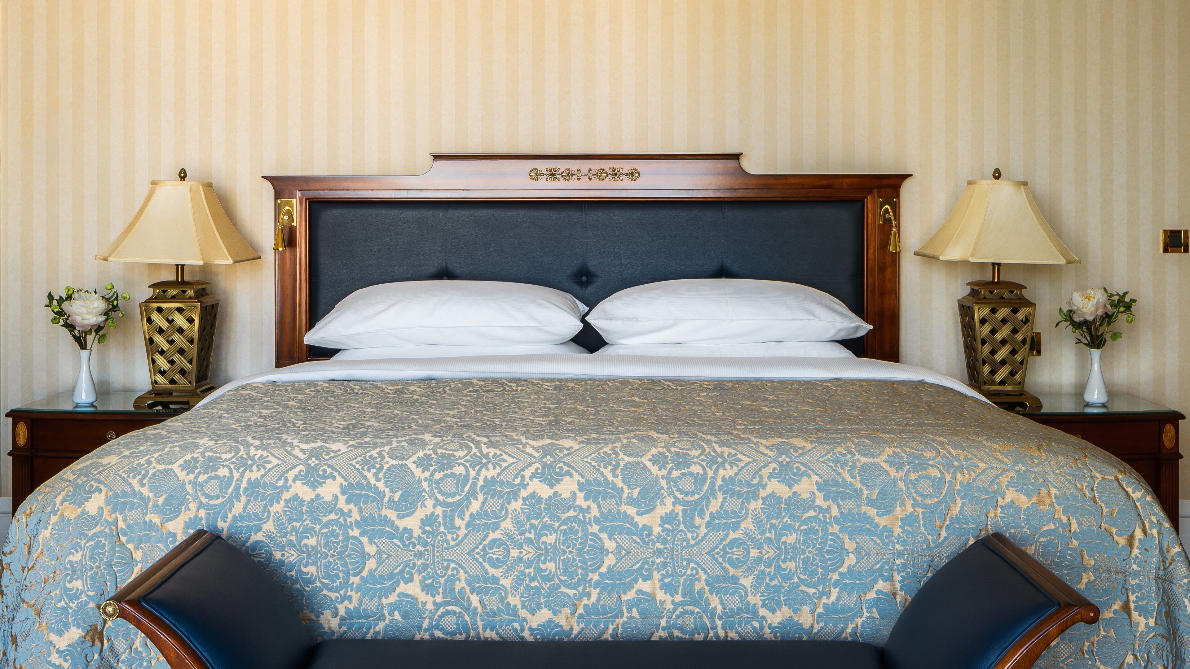 A neatly made bed with a patterned bedspread, two bedside tables with lamps, and a decorative headboard.