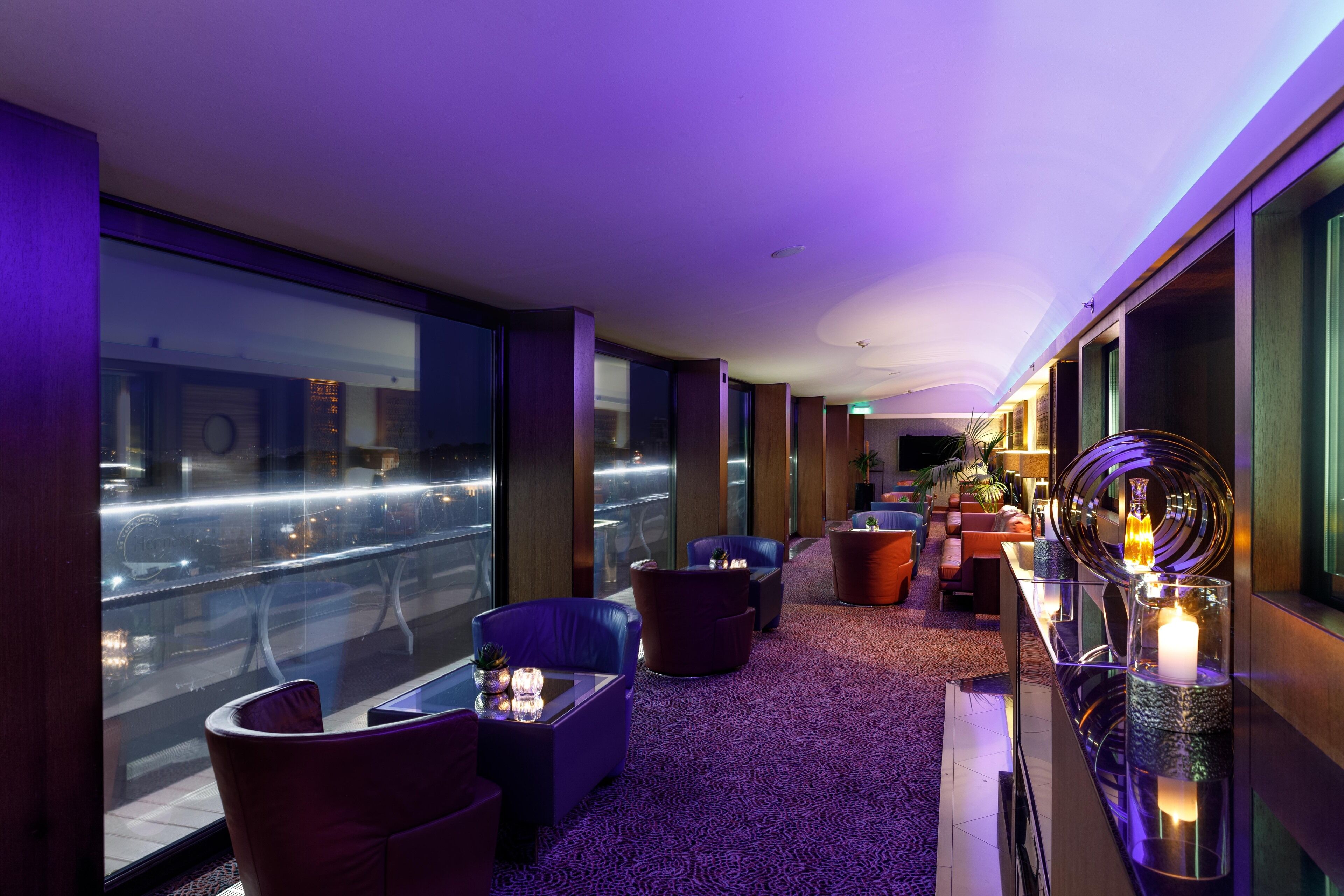 Un hall d’hôtel moderne doté d’espaces de détente, d’un comptoir d’accueil et de grandes fenêtres offrant une vue sur la ville.